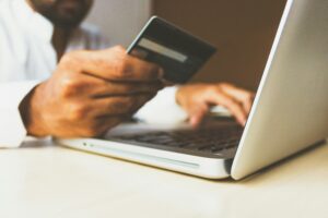 Una persona sostiene una tarjeta de crédito en una mano y escribe en una laptop con la otra, sugiriendo una transacción o compra en línea.